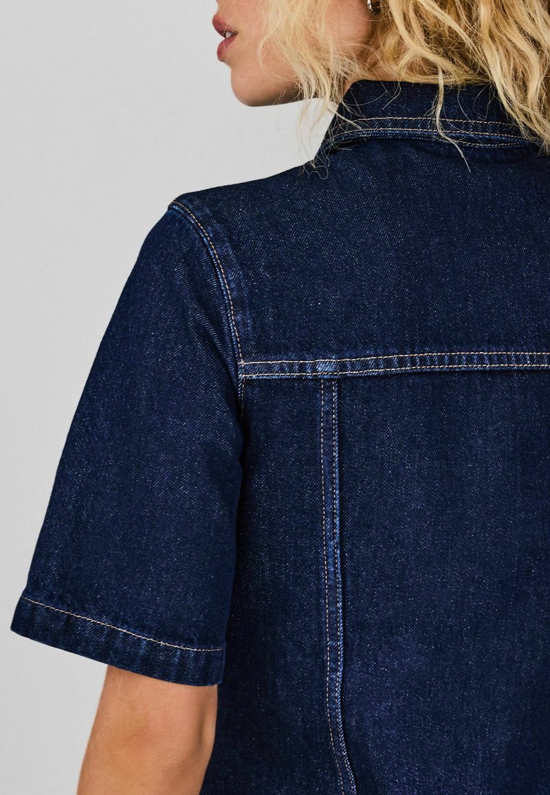 Temno denim srajca s kratkimi rokavi, ki ima klasičen ovratnik, svetlejše šive in detajl jarmu vzdolž hrbta.