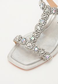 Stříbrné ploché sandály s dekorativními pásky z rhinestones, s designem čtveraté špičky a metalickým povrchem svršku.