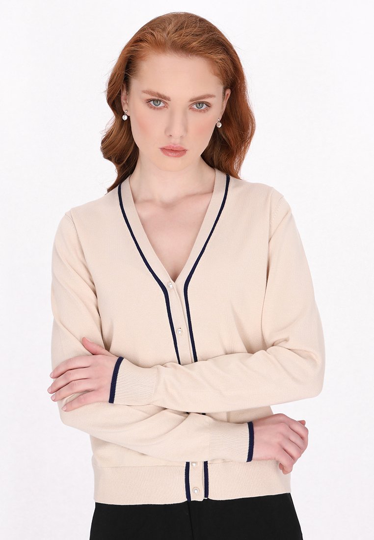 Beige cardigan met marineblauwe afwerking, V-hals en knoopsluiting. Zachte textuur, lange mouwen en geribbelde manchetten. Eenvoudig ontwerp, aansluitende pasvorm.