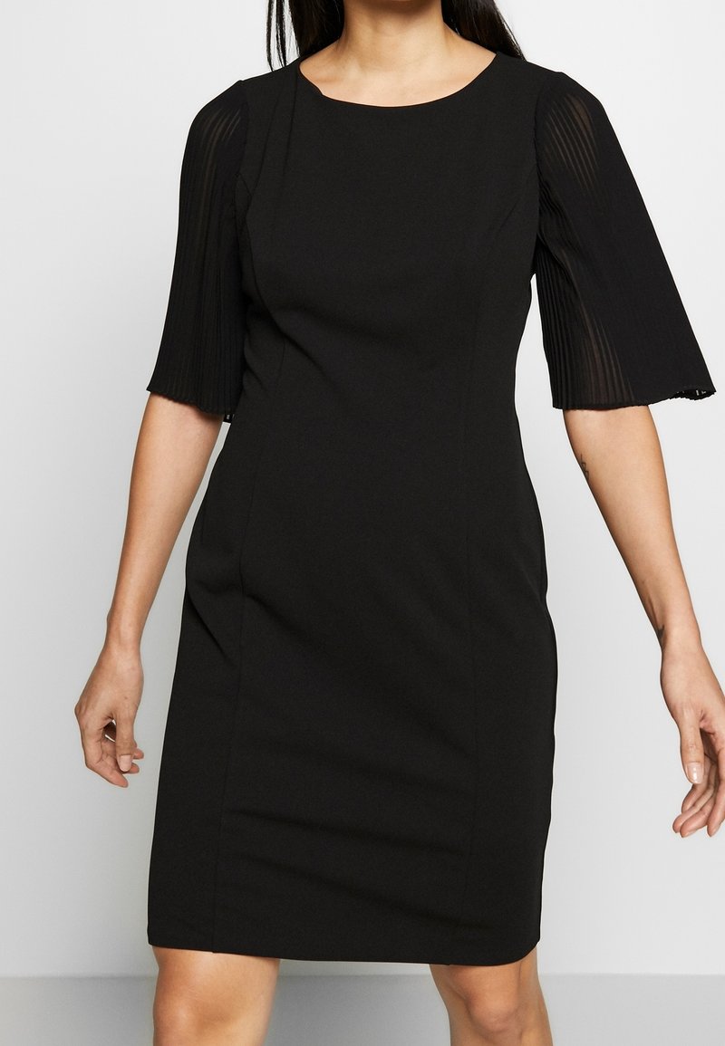 Czarna sukienka z dopasowanym topem i spódnicą do kolan. Posiada krótkie, plisowane rękawy oraz okrągły dekolt. Gładka tekstura, minimalna ilość detali.