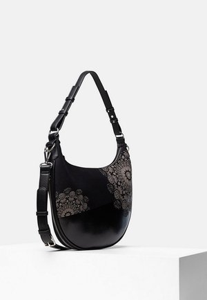 Schwarze Handtasche aus Leder in Mondsichelform mit verstellbarem Riemen und kunstvollen kreisförmigen Blumenmustern vorne, präsentiert auf einem weißen Podest.