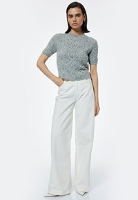 Suéter gris de punto de manga corta con un patrón de trenzado texturizado y adornos plateados, combinado con pantalones anchos blancos.