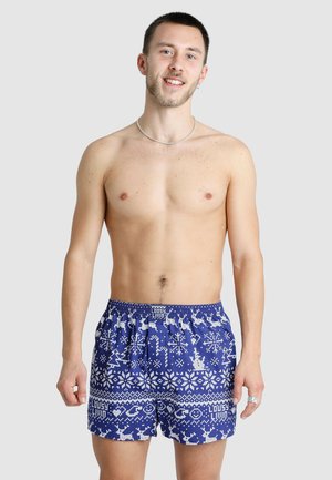 Blaue Badeshorts mit einem festlichen weißen Muster aus Rentieren und Schneeflocken. Elastischer Bund, lockere Passform und keine sichtbaren Taschen.