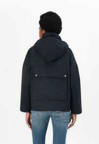 Veste à capuche navy avec une grande poche arrière, dotée d'accents en métal doré et d'une coupe décontractée. Fabriquée à partir d'un matériau texturé et léger.