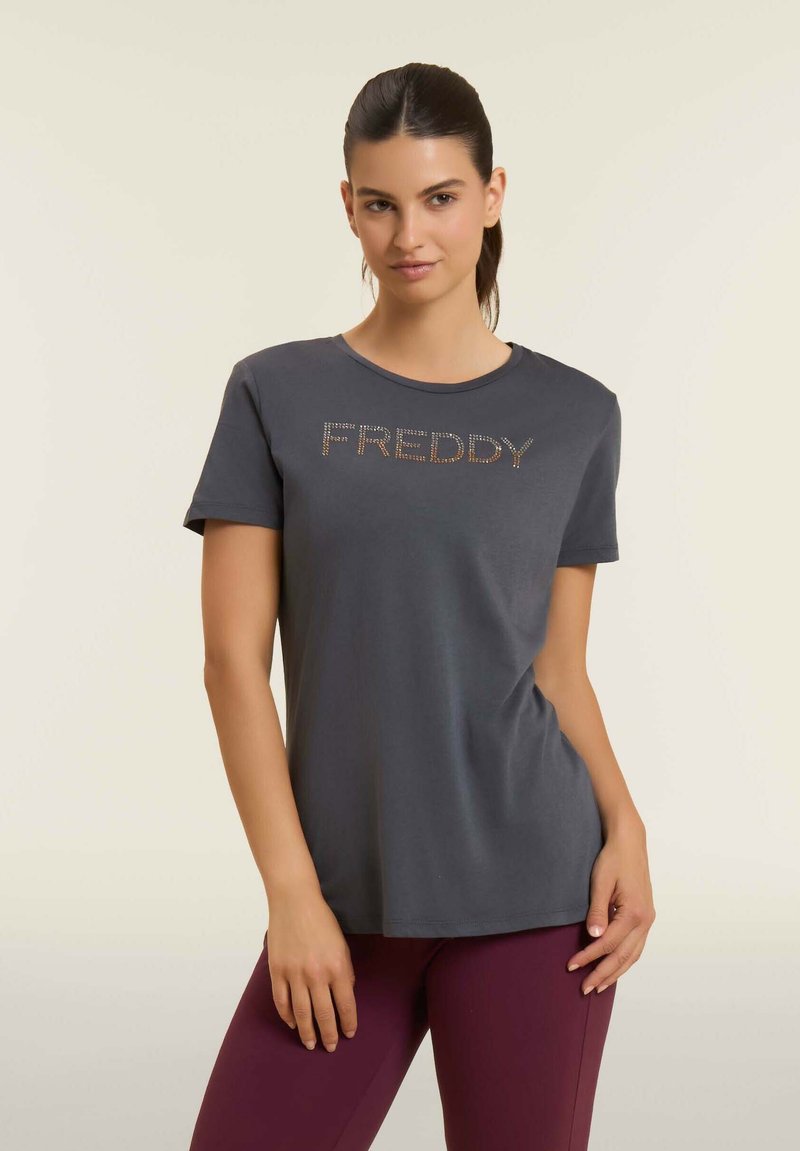 Camiseta de algodón gris con mangas cortas que presenta un logo texturizado de "FREDDY" con acentos brillantes en el pecho. Cuello redondo sencillo.