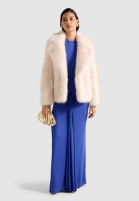 Rosa faux fur frakke med en bred krave, parret med en blå gulvlængde kjole med en knyttet detalje. Guld metallic clutch taske.