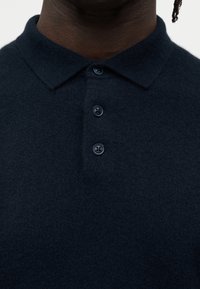 Μπλε πόλο πουκάμισο από απαλό ύφασμα, με κλασικό γιακά και τρεις κουμπότρυπες. Διαθέτει υφή και διακριτικές ραφές.