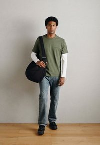 Vihreä puuvillainen T-paita valkoisen pitkähihaisen paidan päällä, yhdistetty vaaleansinisiin farkkuihin ja mustiin tennareihin. Musta olkalaukku on yli olan kannettuna.