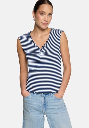 Femme portant un haut sans manches rayé marine et blanc avec un col et un ourlet festonnés, assorti à un jean en denim bleu clair.