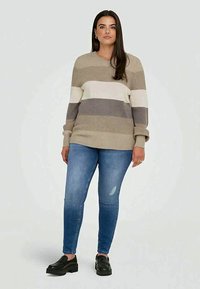 Jersey a rayas en beige, crema y gris; textura acanalada; escote redondo. Combinado con jeans skinny azules y mocasines negros.