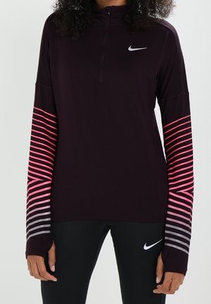 Femme portant un haut de sport noir à manches longues avec des manches rayées roses et grises et un legging noir, tous deux arborant des logos Nike blancs.
