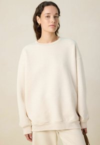 Sweatshirt oversize beige clair avec un col rond, des coutures d'épaule tombantes et des poignets côtelés. Fabriqué en tissu doux et texturé.