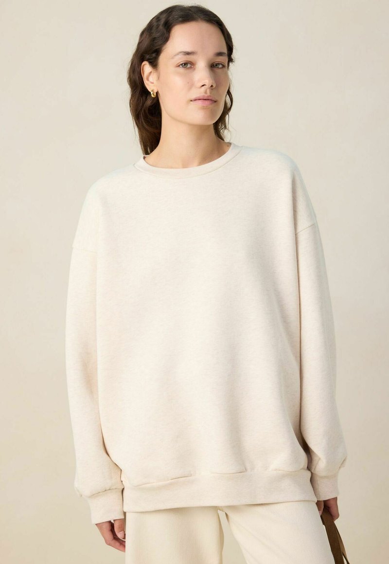 Sweatshirt oversize beige clair avec un col rond, des coutures d'épaule tombantes et des poignets côtelés. Fabriqué en tissu doux et texturé.