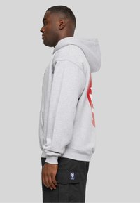 Grau gehäuftes Sweatshirt mit einer vorderen Tasche, herabgesetzt Schultern und einem großen roten Grafik auf dem Rücken. Strukturierten Stoff mit gerippten Bündchen.