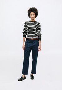 Ριγέ μαύρο και άσπρο πουλόβερ με μακριά μανίκια, συνδυασμένο με ναυτικό μπλε παντελόνι και καφέ ζώνη. Μαύρα μοκασίνια ολοκληρώνουν την εμφάνιση.