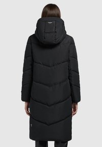 Svart puffjacka med huva, med chevron-quilting, lång silhuett och en liten logotyp på nederkanten. Slät tygtextur.