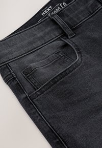 Nahaufnahme von schwarzen Denim-Jeans mit Vordertasche, kleiner Münztasche mit Nieten, Gürtelschlaufe und Taillenetikett.