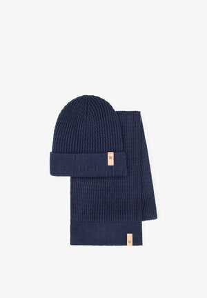 Marineblauwe gebreide muts en sjaal set met geribbelde textuur. De muts heeft een opgevouwen boord en beide items zijn voorzien van een klein leren merketiket.