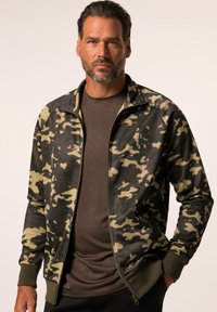 Camouflage trui met rits in donker groen en beige, met ribbels voor de manchetten en kraag, gelaagd over een donkerbruine shirt, aansluitend ontwerp.