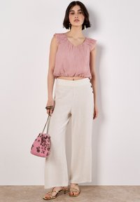 Top plettato rosa scuro con spalline arricciate, abbinato a pantaloni larghi color crema con bottoni laterali e una borsa rosa ricamata. Sandali dorati.