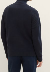 Maglione lavorato a maglia blu navy con colletto alto, caratterizzato da dettagli a costine testurizzati sulle spalle e sui polsini, e una finitura liscia sul corpo.