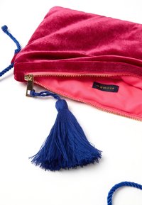 Borsa in velluto rosa con cerniera dorata, interno rosa brillante e un accento in frangia blu. Include una maniglia in corda blu attorcigliata.