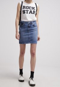 Vit ärmlös skjorta med "ROCK STAR" i svart text, blå denimminikjol, svarta prickiga strumpor och vita skor med svarta sulor.