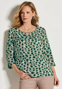 Groen en beige top met een luipaardprint, ronde halslijn en driekwartmouwen. Heeft een sleufdetails aan de voorkant.