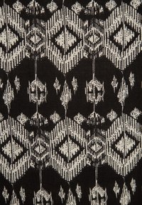 Tessuto nero con un motivo geometrico di diamanti bianchi e frecce, con texture di punti variabili che creano profondità e contrasto.