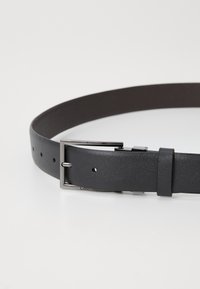 Schwarzer Leder Gürtel mit strukturiertem Finish, ausgestattet mit einer silbernen rechteckigen Schnalle aus Metall und mehreren Einstelllöchern.