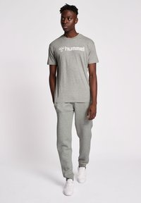 Grijze katoenen t-shirt met het "hummel" logo, gecombineerd met bijpassende grijze joggingbroek. Model draagt witte sneakers, wat een ontspannen pasvorm en stijl laat zien.