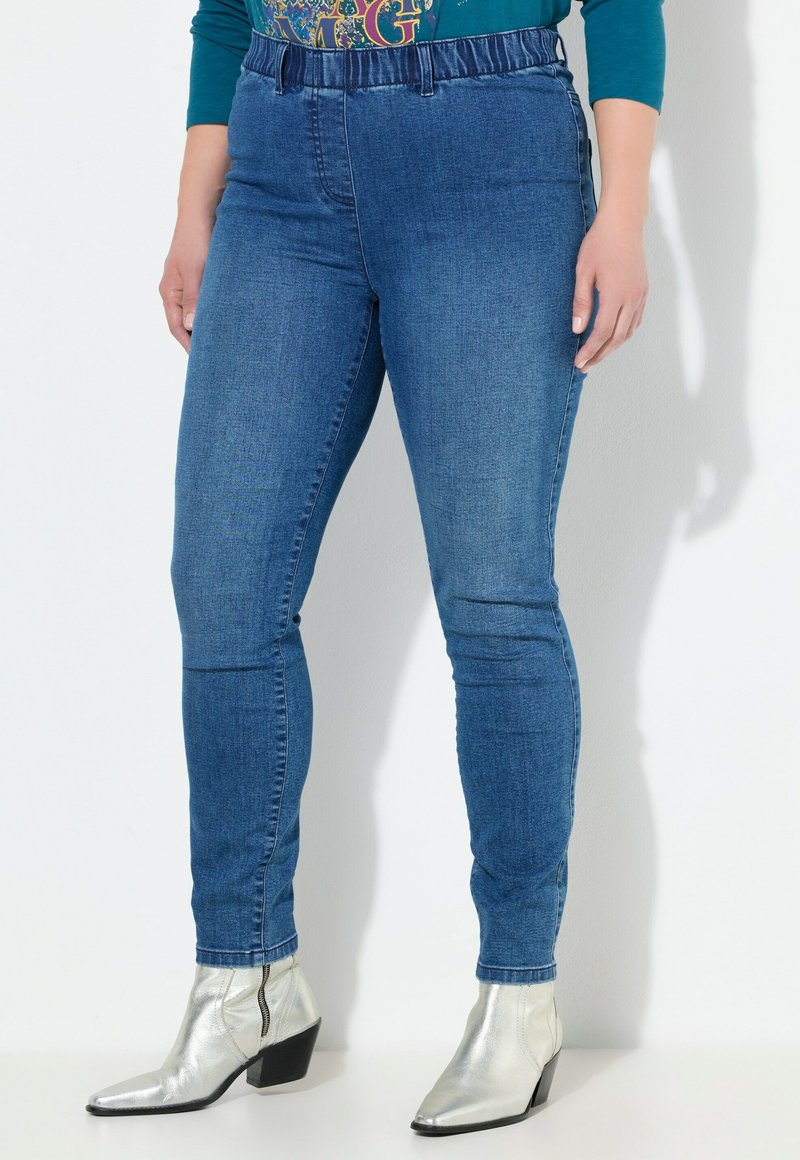 Modré džíny z denimu se strečovým pasem, s úzkým střihem a minimálním prošitím. V kombinaci se stříbrnými kozačkami na podpatku.
