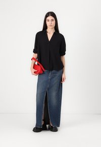 Black collared blouse, long denim skirt with front slit, and red handbag. Model wears black chunky shoes. Simple background.