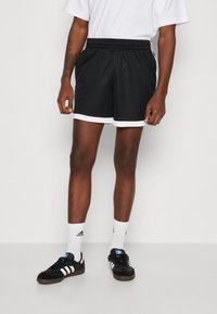 Zwarte mesh shorts met een witte tailleband en randen. Gemaakt met zwarte Adidas sneakers en witte crew sokken met het Adidas logo.