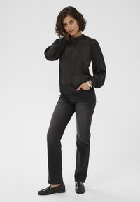 Bluză din satin negru cu mâneci bufante, guler strâns, asociată cu blugi închiși la culoare și loafers negri, având un design simplu și elegant.