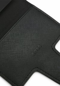 Zwarte leren kaarthouder met een getextureerd oppervlak, voorzien van een uitsnede en geperst merklogo. Gestikte randen benadrukken het ontwerp.