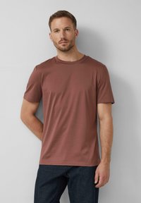 Tee s krátkym rukávom v hnedej farbe z bavlny s okrúhlym výstrihom; mäkká textúra; nosené s tmavými džínsami; jednoduchý dizajn bez vzorov.