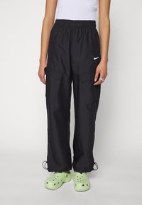Zwarte cargobroek met een elastische taille, twee grote zijzakken, verstelbare broekspijpen met een koord en een klein wit Nike-logo op de linkerdij.