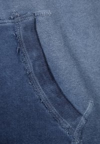 Mörkblått tyg med mjuk textur har en ficka med slitna kanter. Sömmarna är synliga, vilket ger detalj till plagget.