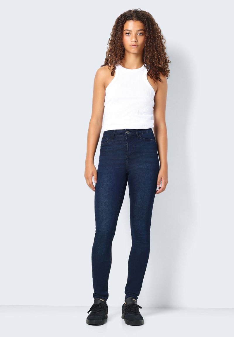 Mörkblå högmidjade jeans i denim med en figursydd design och fem fickor, i kombination med en vit ribbad linne.