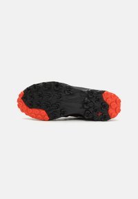 Schwarze Sport-Schuhsohle mit roten Akzenten, ausgestattet mit einem multidirektionalen Stollenmuster für Traktion und Haltbarkeit. Das Material wirkt gummiert.