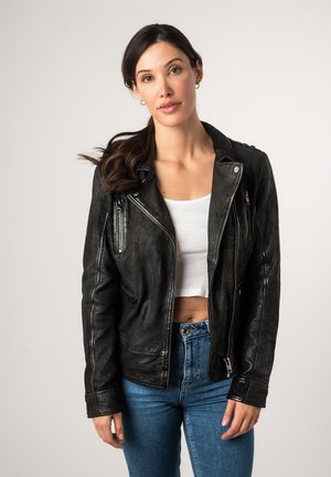 Schwarze Leder-Bikerjacke mit silbernem Beschlag, Reißverschlusstaschen und einer leicht strukturierten Oberfläche. Getragen über einem weißen Crop-Top.