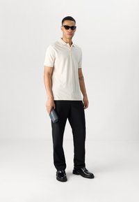 Polohemd in hellbeige, taillierte Passform; kombiniert mit schwarzen Hosen. Accessoires umfassen elegante, quadratische schwarze Sonnenbrillen und eine marineblaue Geldbörse.