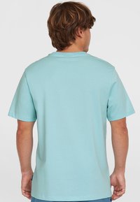 Svetlo modra majica s kratkimi rokavi iz mehkega bombažnega materiala. Ima klasičen okrogel izrez in ravno obrobo ter nalepko na spodnjem levem delu.