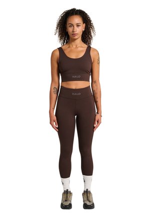 Bruine sportbh met brede banden en logo, gecombineerd met bijpassende hoge legging. Tan wandelschoenen en witte sokken maken de outfit compleet.