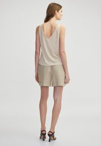 Top sin mangas beige con espalda en V, combinado con pantalones cortos de color claro con dobladillos enrollados. La modelo también lleva tacones negros con tiras.