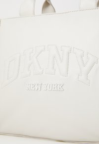 Weiße Leder-Tote-Tasche mit geprägtem "DKNY"-Logo und "NEW YORK"-Text, mit subtilen Nähten und zwei oberen Griffen.
