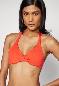 Rød bikinitopp med halterneck-design, laget av glatt stoff. Har et tvistet aksent i midten og brede stropper for støtte.