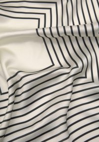 Hedvábná tkanina s krémovým pozadím, na kterém se nacházejí výrazné černé linky uspořádané v různých šířkách a geometrických tvarech, které vytvářejí hloubku a texturu.