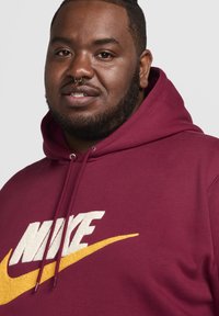 Sudadera de Nike en color burdeos con un logo blanco y amarillo. Cuenta con una capucha ajustable y letras texturizadas. Tejido suave con un corte relajado.